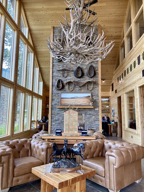 Rock fireplace decorated with horse wagon yokes, tan leather furniture and elk shed chandelier greet guests open arrival at Silvies Valley Ranch Gate House in Seneca, Oregon.